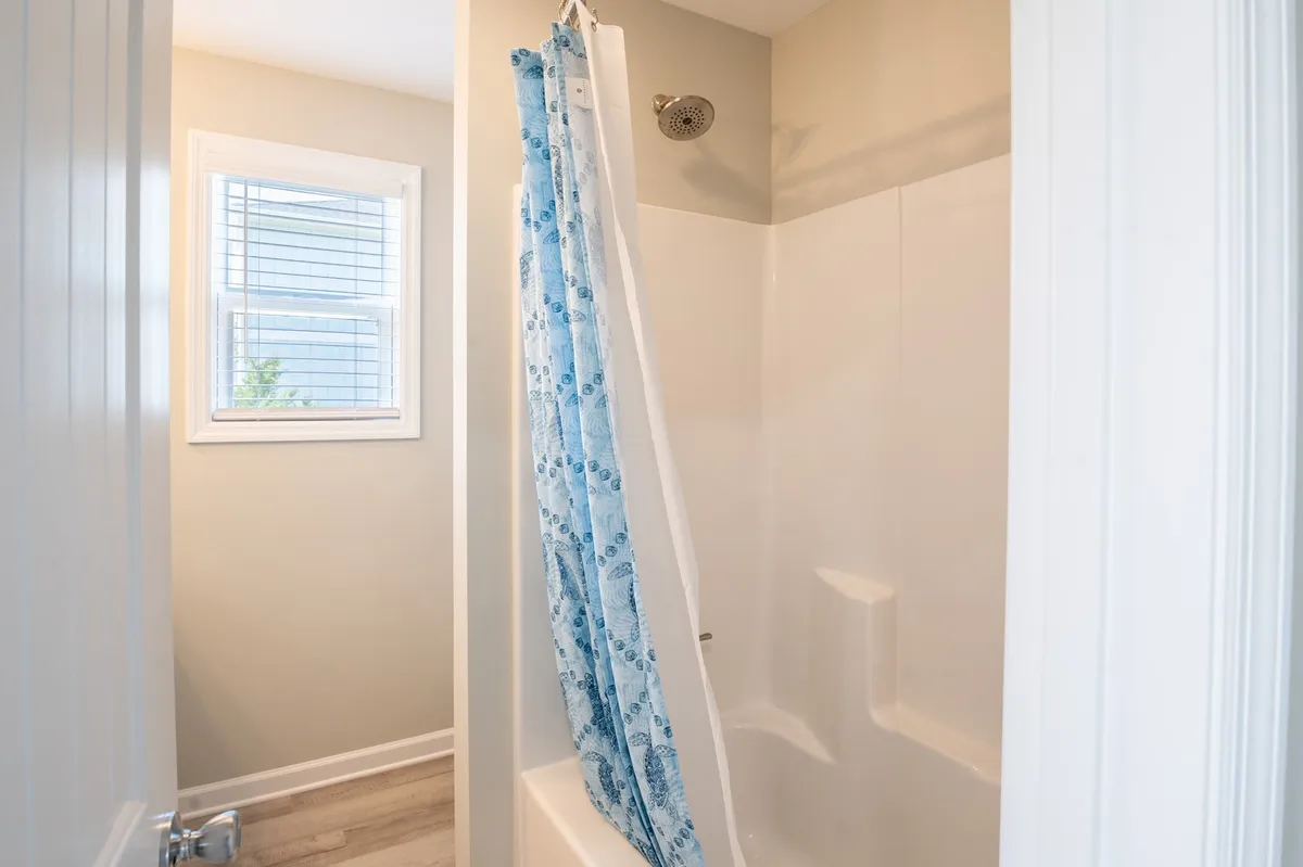 A bright, inviting shower space with a simple shower curtain, window, and showerhead. The space feels fresh and functional, ideal for rinsing off after a day at the beach.