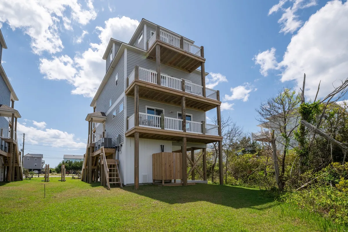 A wide exterior view of a three-story vacation home with expansive balconies and a green lawn, inviting outdoor gatherings, sunbathing, and relaxing with pets. The decks offer ample outdoor space for enjoying sea breezes and precious moments with your pup.
