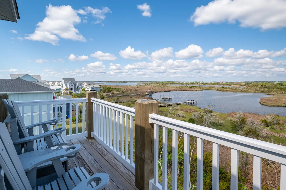 A tranquil deck with adirondack chairs overlooking a peaceful sound, under a soft, cloudy sky. The wide water vista and inviting seating capture the relaxation and connection to nature available in the evenings.