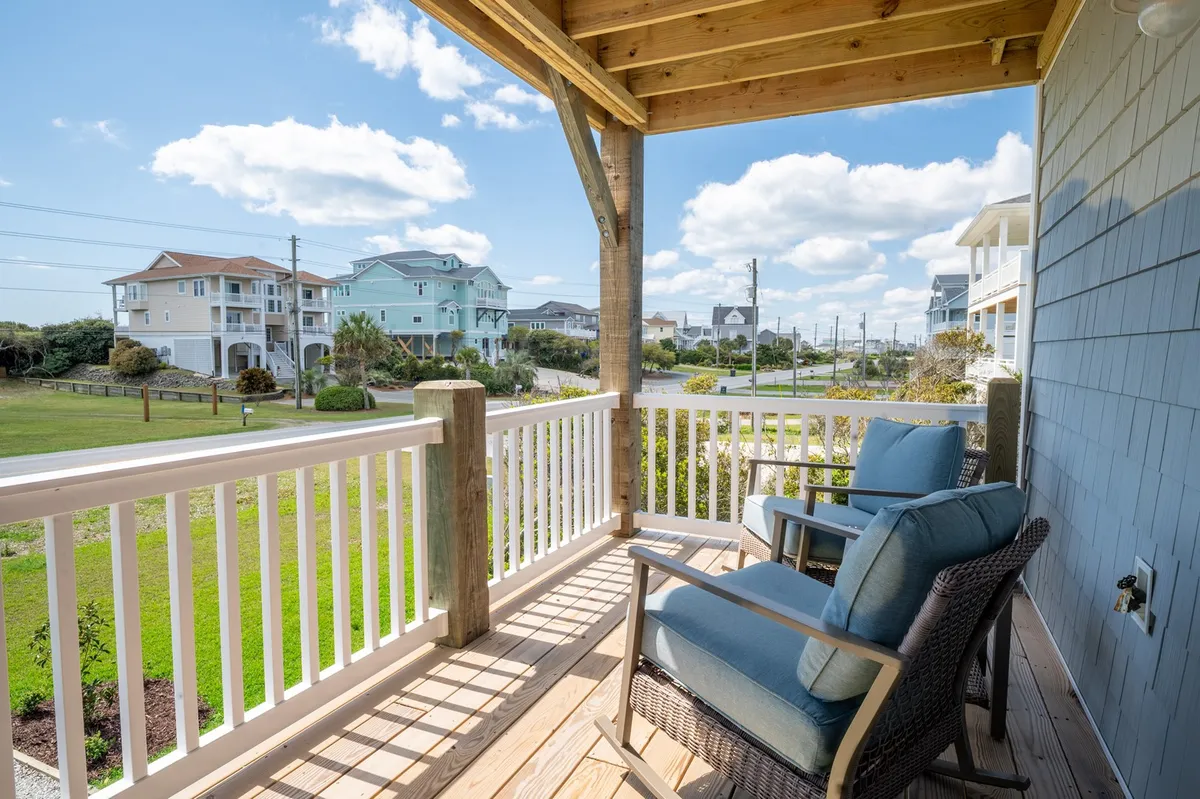 A serene exterior shot featuring blue chairs positioned on a wooden deck, overlooking the surrounding neighborhood. The view invites guests to relax and enjoy the scenery, with expansive sky and hints of local wildlife visible at the edges.