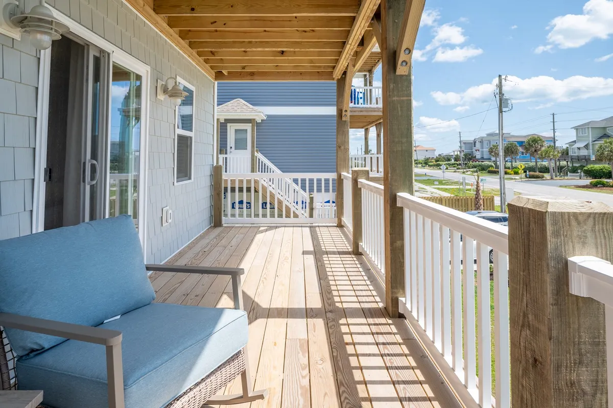 A tranquil exterior porch scene featuring a blue armchair and a wide wooden railing, with plenty of space to relax, enjoy the view, or share quiet moments with your pet after a day at the beach.