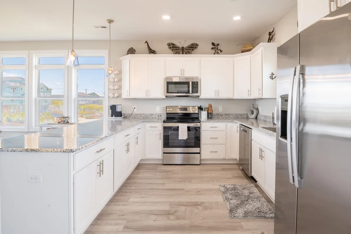 A bright, open kitchen with granite countertops, stainless steel appliances, and large windows that fill the space with natural light. The kitchen is perfectly laid out for cooking and entertaining, with plenty of workspace and a view across to the dining and living areas.