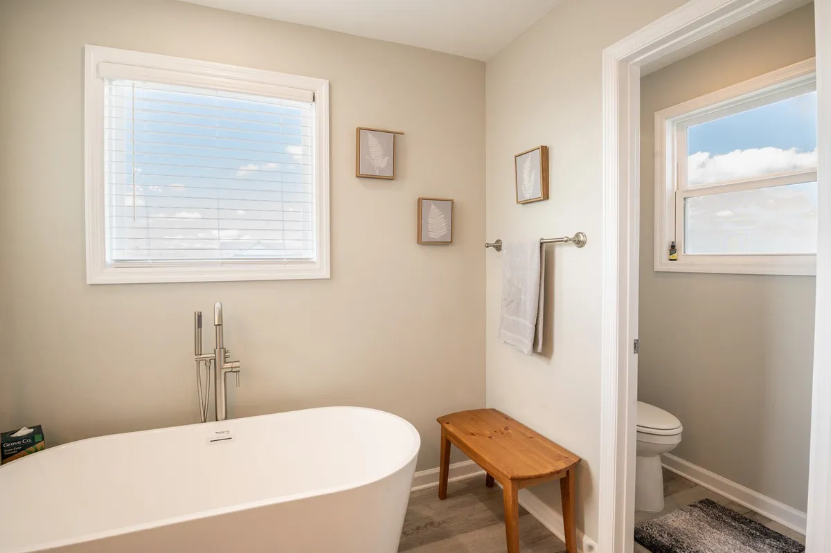 A tranquil bathroom with a freestanding soaking tub, wooden bench, and soothing decorative accents. The space exudes a spa-like ambiance, inviting relaxation and self-care.